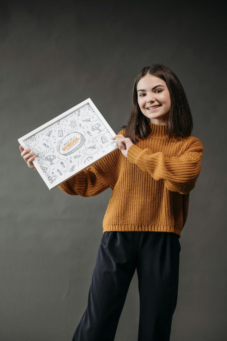 A teenage girl smiling while holding an artistic illustrated poster in a studio setting.