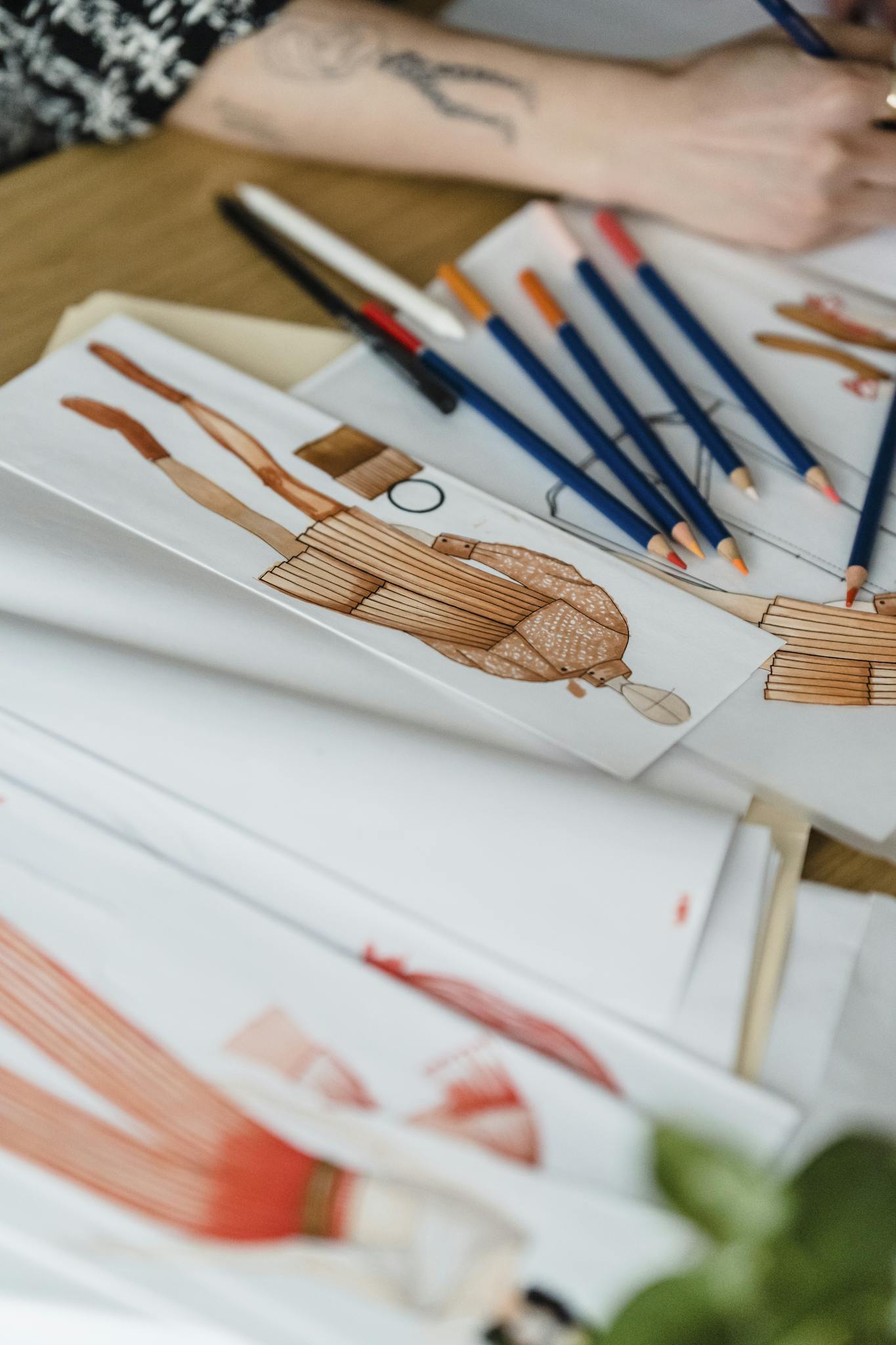 Close-up of fashion design sketches with pencils on a designer's desk.