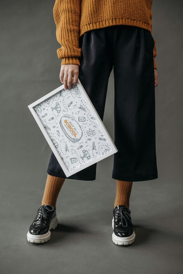 Fashionable adult holding a school-themed poster against a gray background, showcasing a casual style.