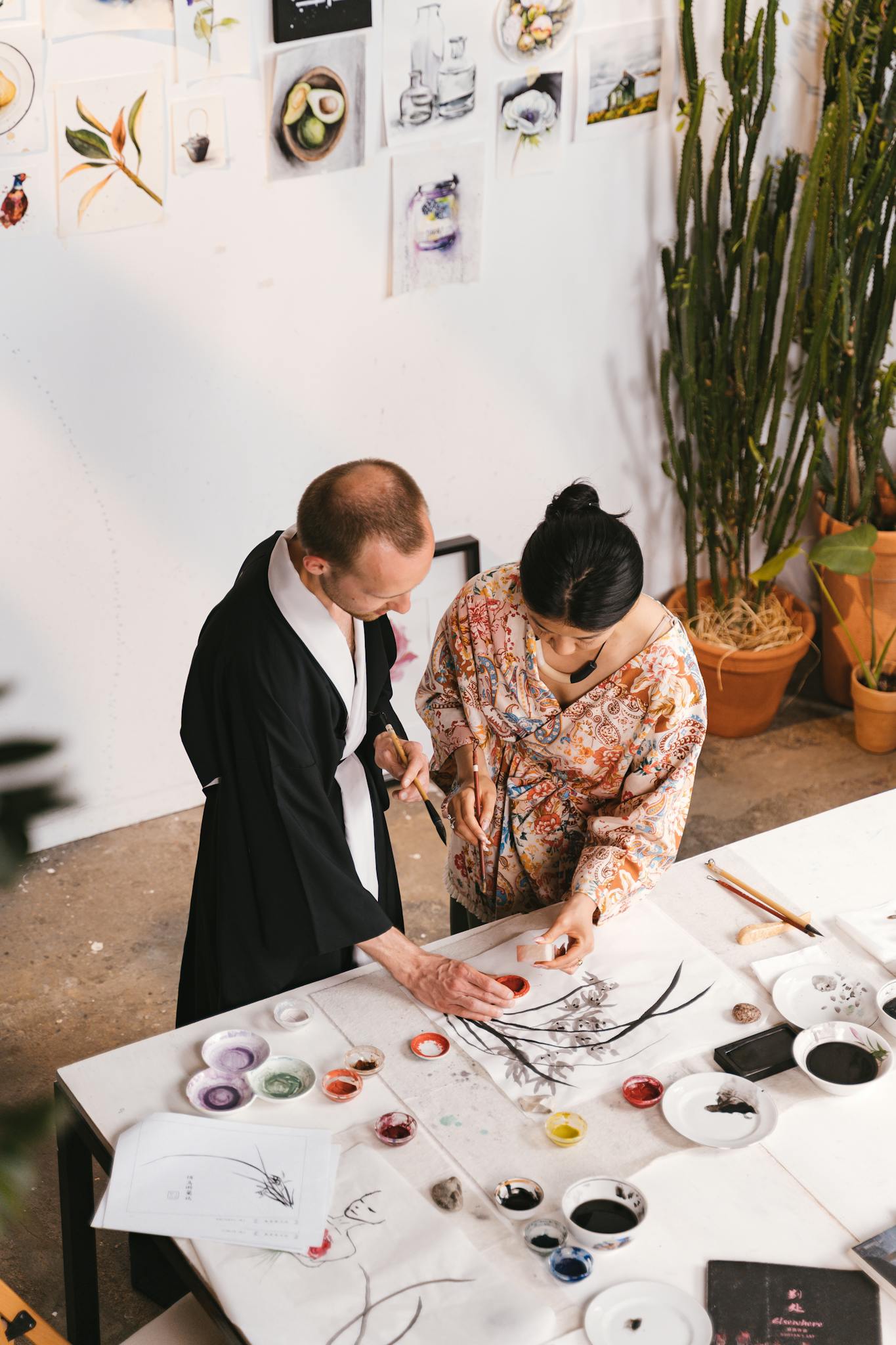 Two adults practicing calligraphy with guidance in a bright studio setting.