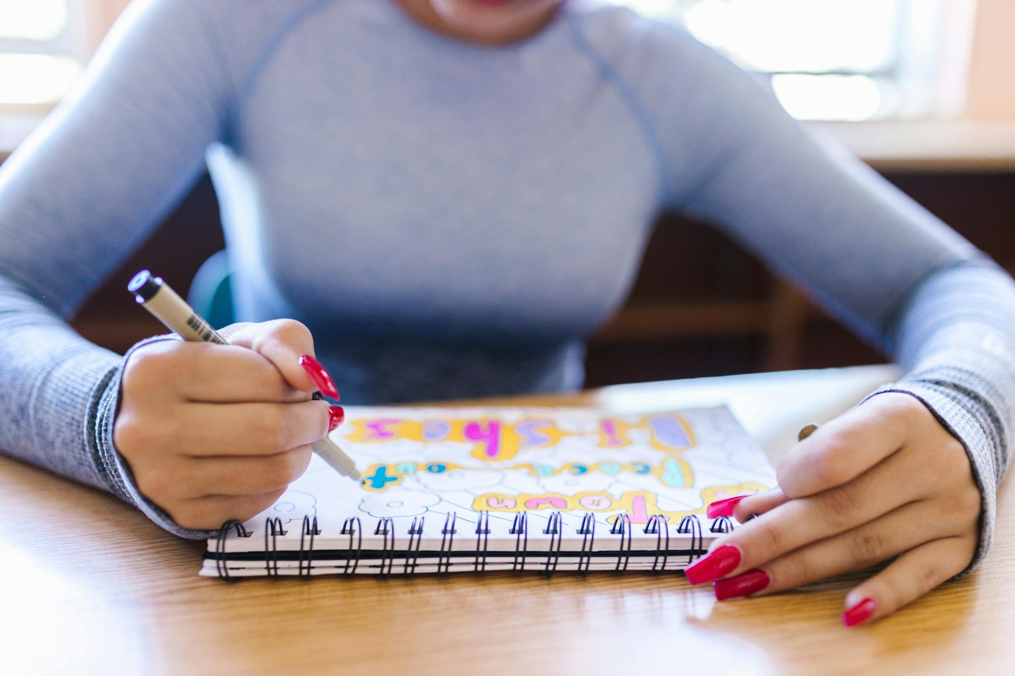 Woman drawing in a notebook with colorful pens in an indoor setting, showcasing creativity and focus.