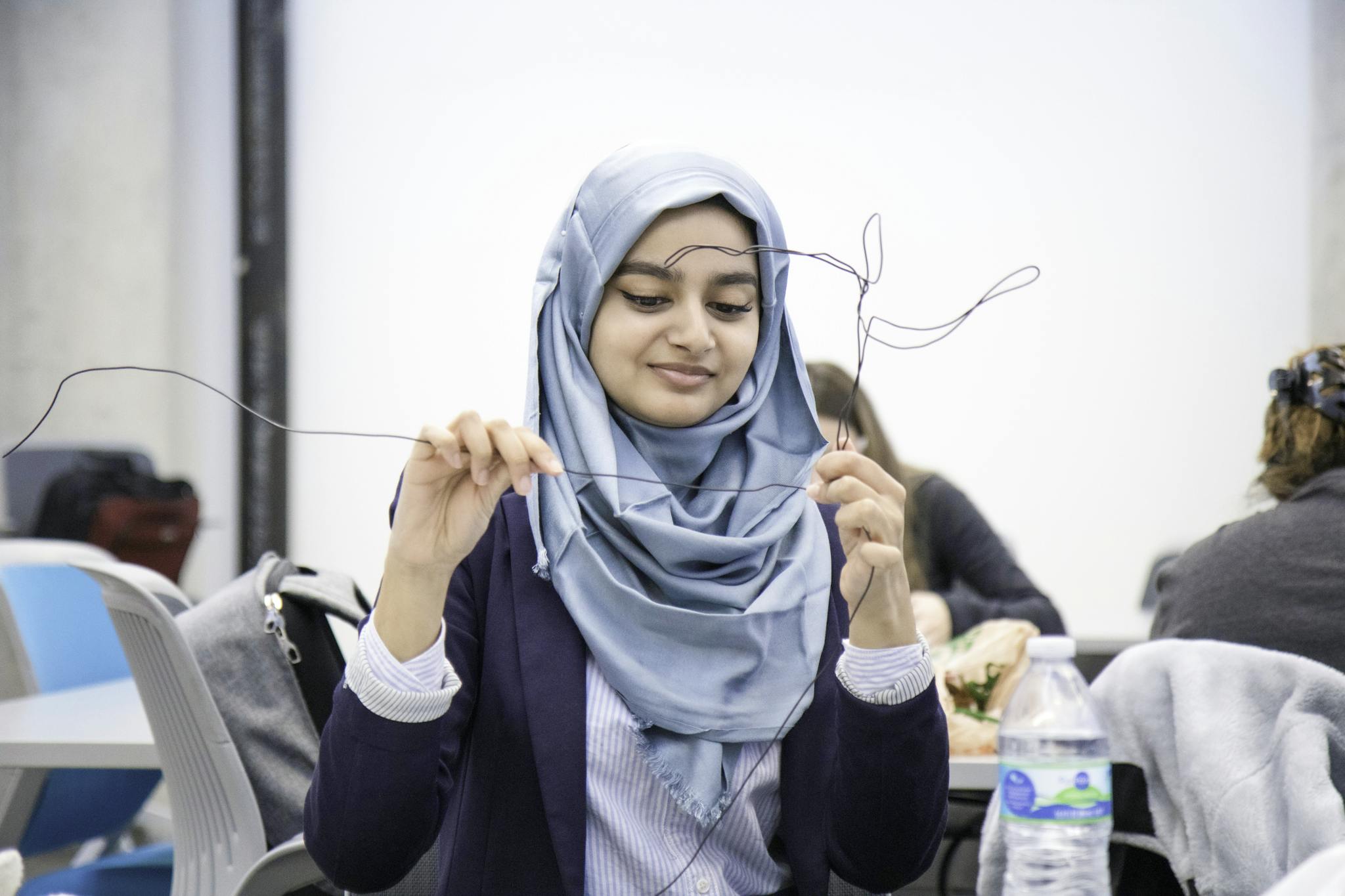 Young woman in a hijab involved in a creative wire art project during an art class.